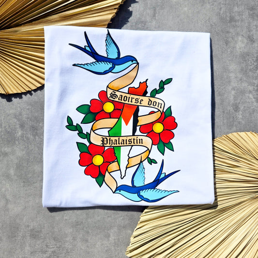 White shirt with colorful tattoo-style design featuring birds, flowers, and a banner saying Saoirse don Phalaistín.