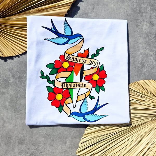 White shirt with colorful tattoo-style design featuring birds, flowers, and a banner saying Saoirse don Phalaistín.